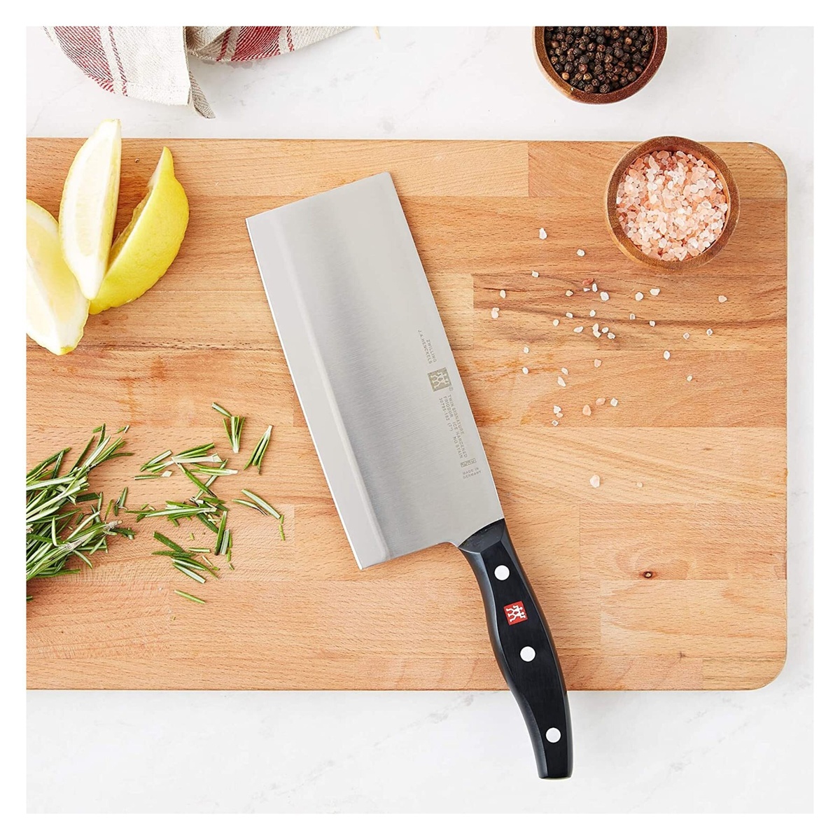 Zwilling Signature 7-inch Chinese Chef's Knife on a wooden cutting board with sliced lemons and rosemary.