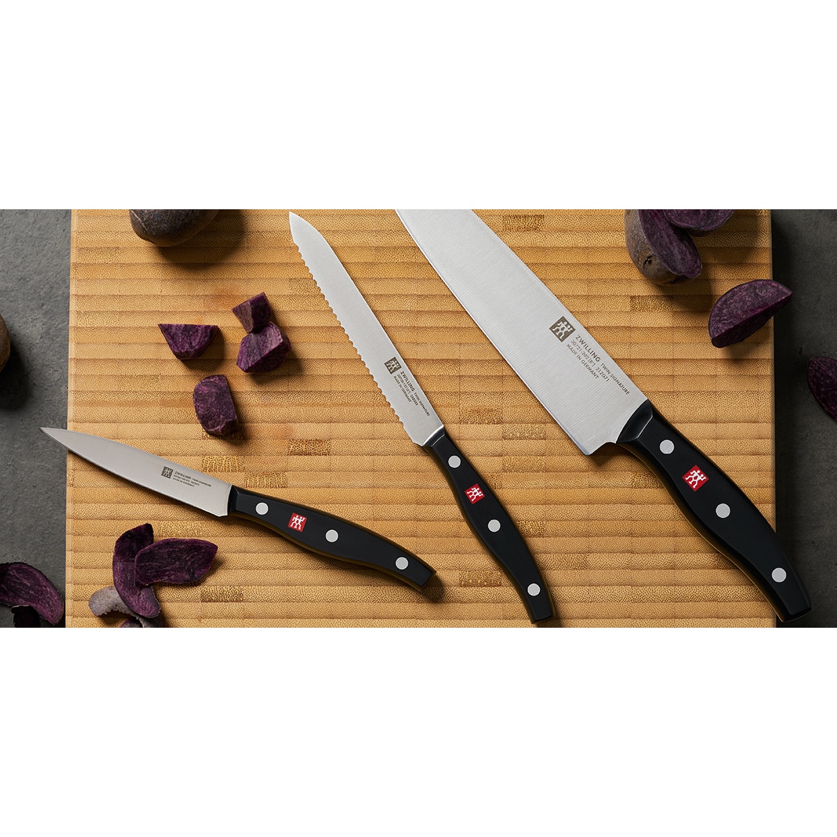 A collection of Zwilling Signature knives including a chef's knife and paring knife on a bamboo cutting board.