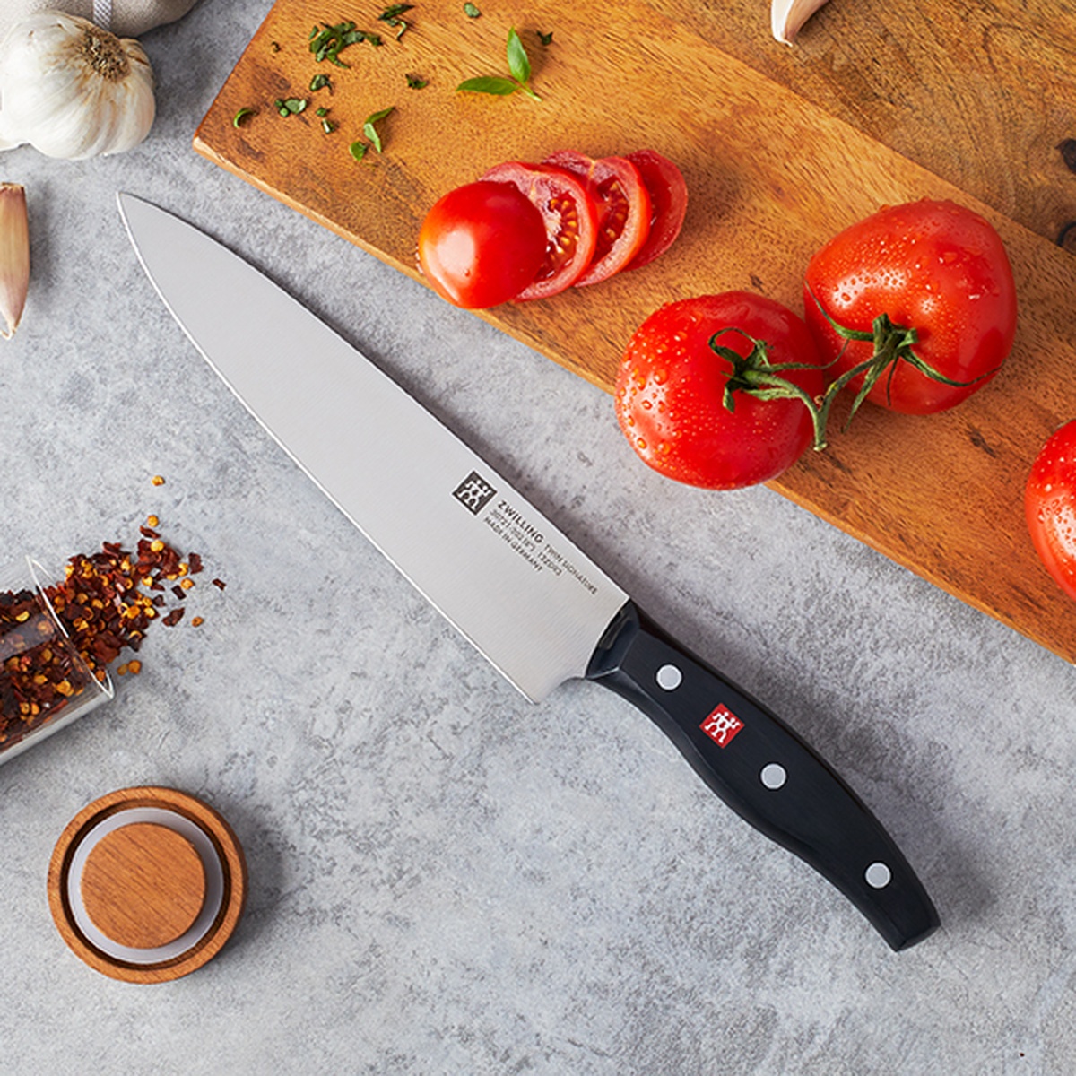 Zwilling Signature knife on a wooden cutting board next to fresh tomatoes and spices.