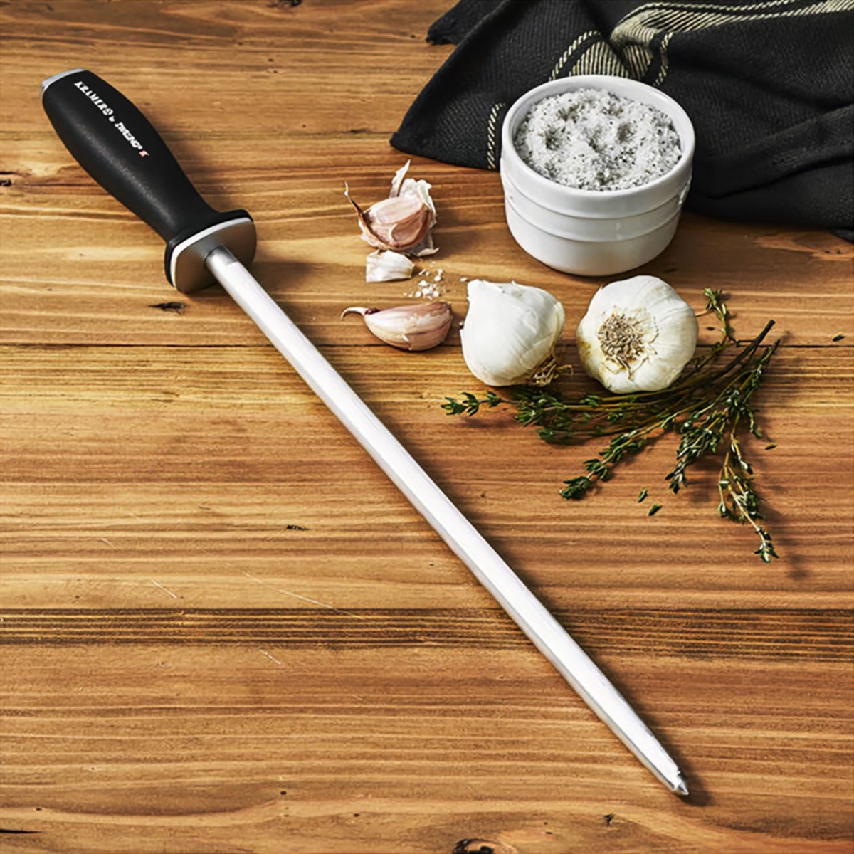 Honing steel resting on a wooden cutting board with garlic and herbs