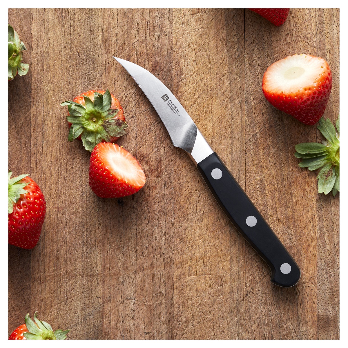 Zwilling Pro bird's beak peeling knife on a wooden cutting board with fresh strawberries