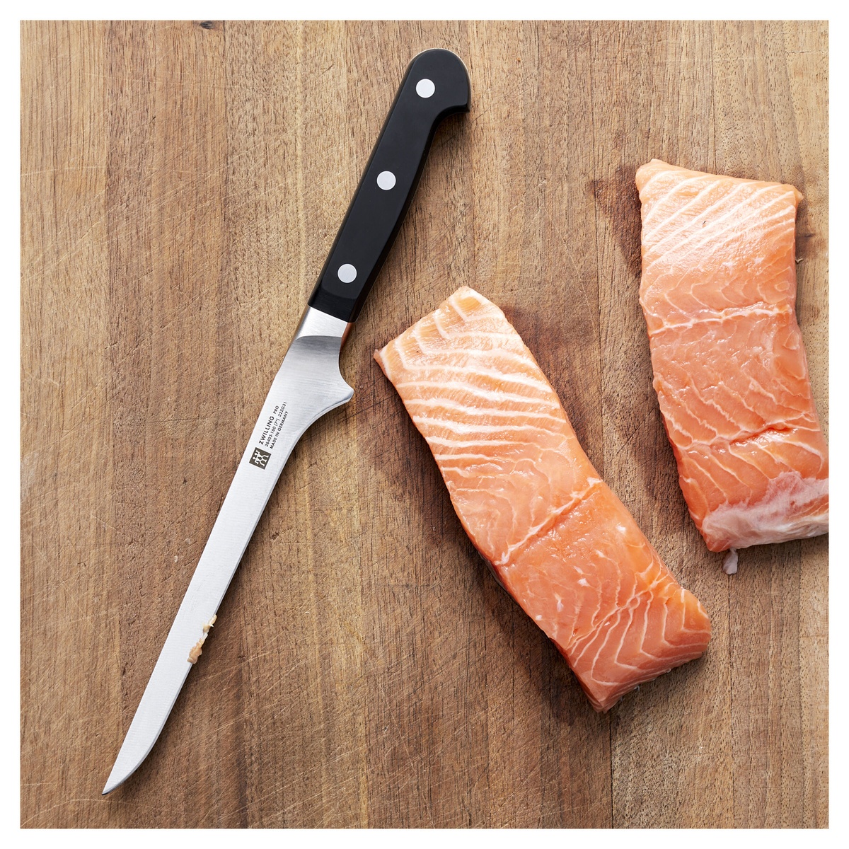 Zwilling Pro 7-inch fillet knife resting on a wooden cutting board next to fresh salmon fillets
