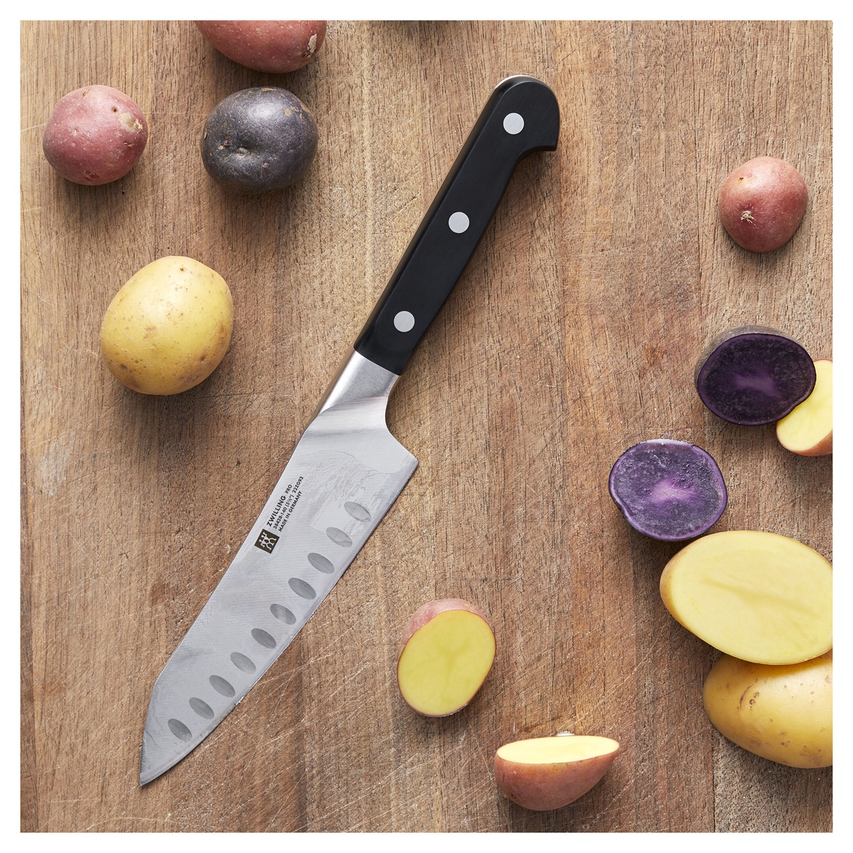 Zwilling Pro Santoku knife on a wooden cutting board with sliced potatoes