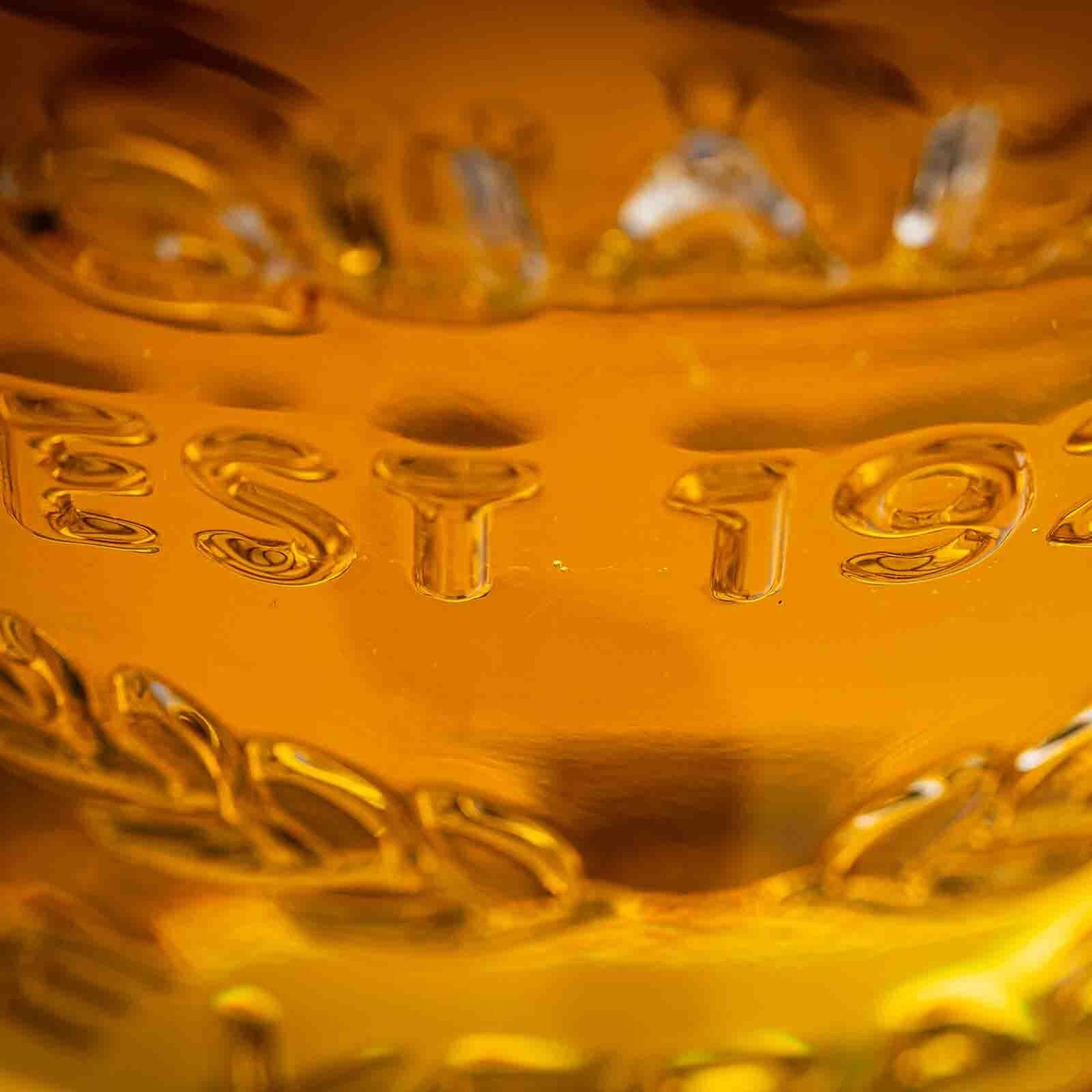 Close-up of embossed EST 19 text detail molded into the clear glass body of the TableCraft Industrial Collection beverage dispenser