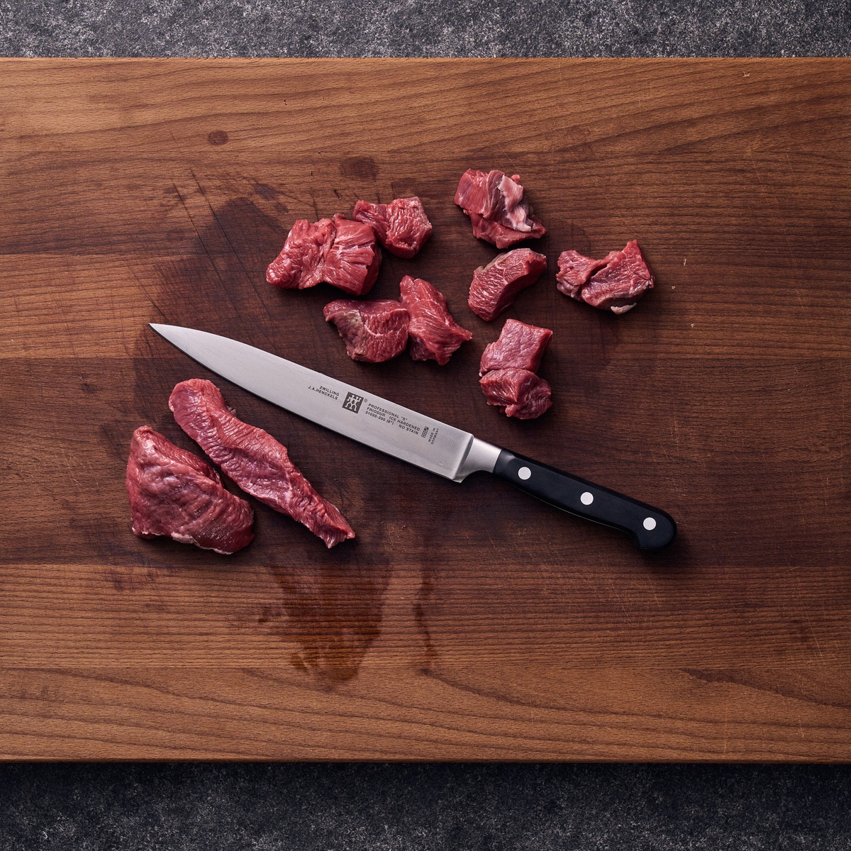 Zwilling Professional S slicing knife on a wooden cutting board with raw meat