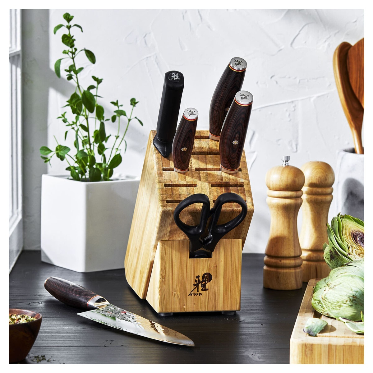 Miyabi Artisan knife block set on a dark kitchen counter with artichokes