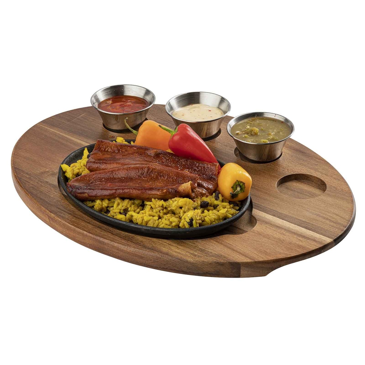Angled view of oval acacia wood fajita serving board with three stainless ramekins of sauces and cast iron sizzle platter with grilled meats and rice