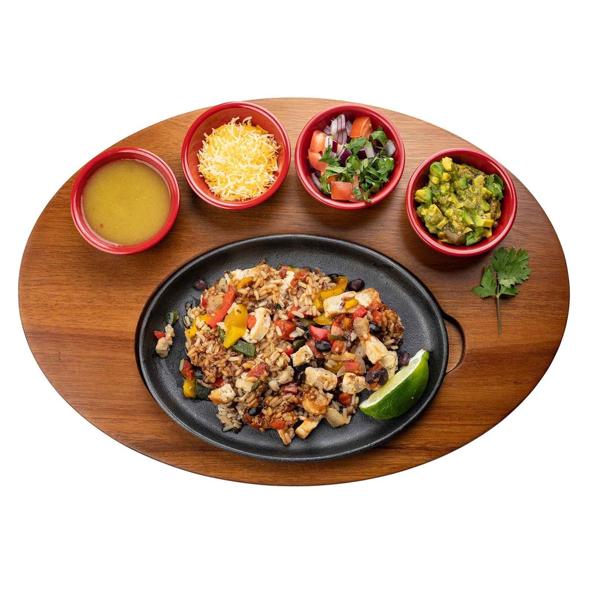 Oval acacia wood serving board top-down view loaded with sizzle platter of chicken fajita mix and four ramekins of toppings