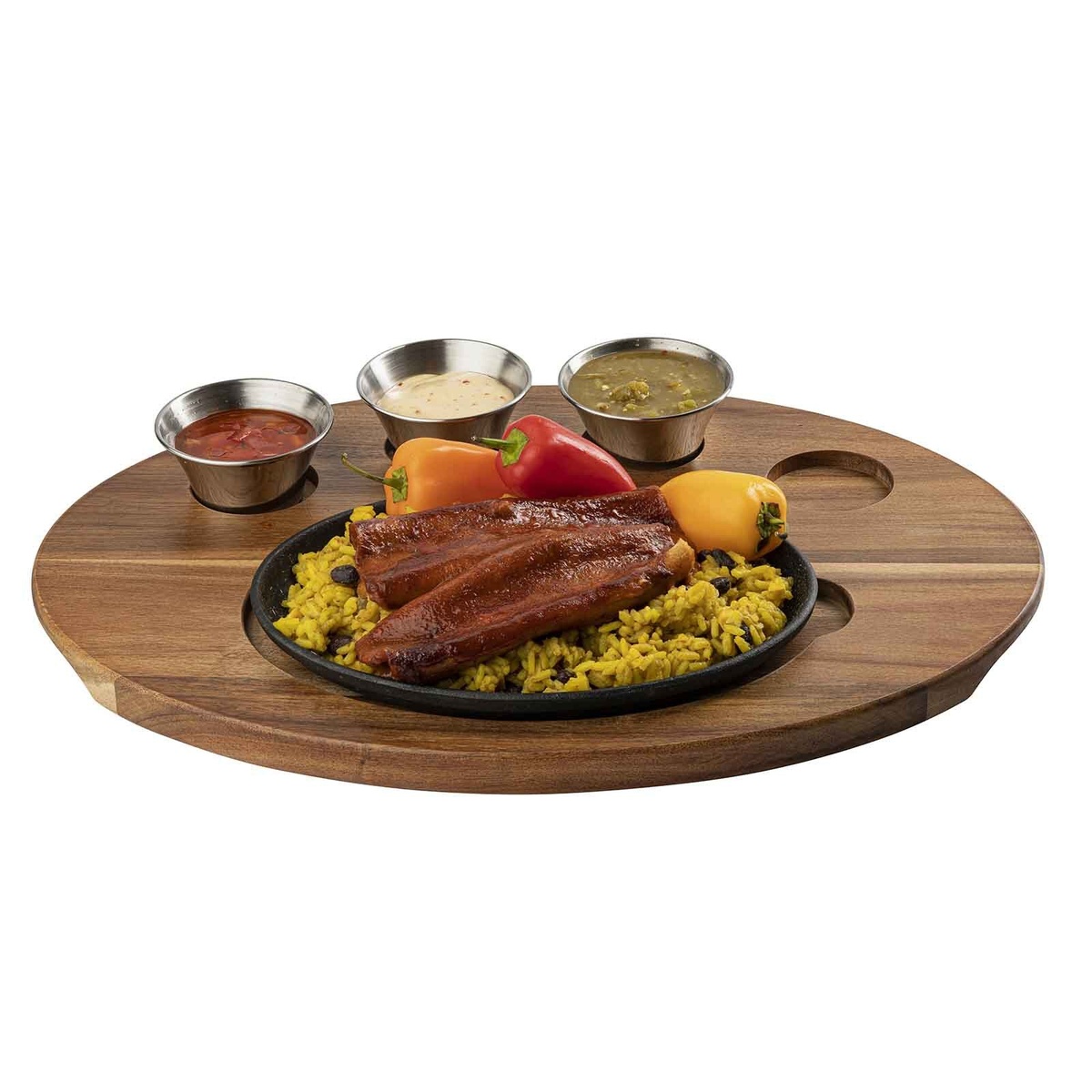 Angled overhead view of oval acacia wood serving board holding cast iron sizzle platter with fajita meats and rice alongside three stainless ramekins with sauces