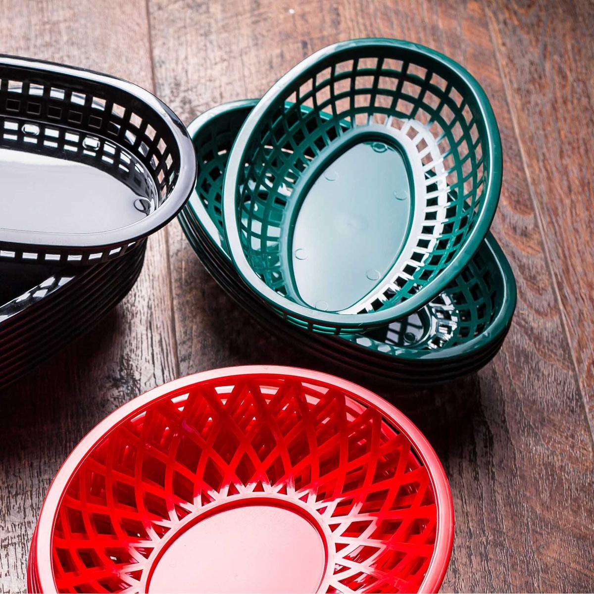 Multiple stacked green, black, and red TableCraft classic plastic serving baskets displayed on a wooden surface