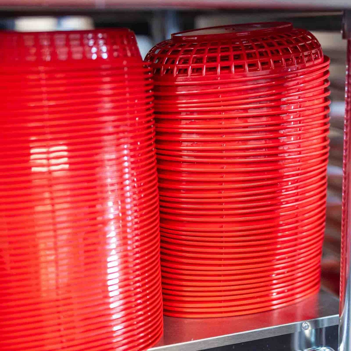 Large stacks of red oval plastic serving baskets stored on a metal shelving unit