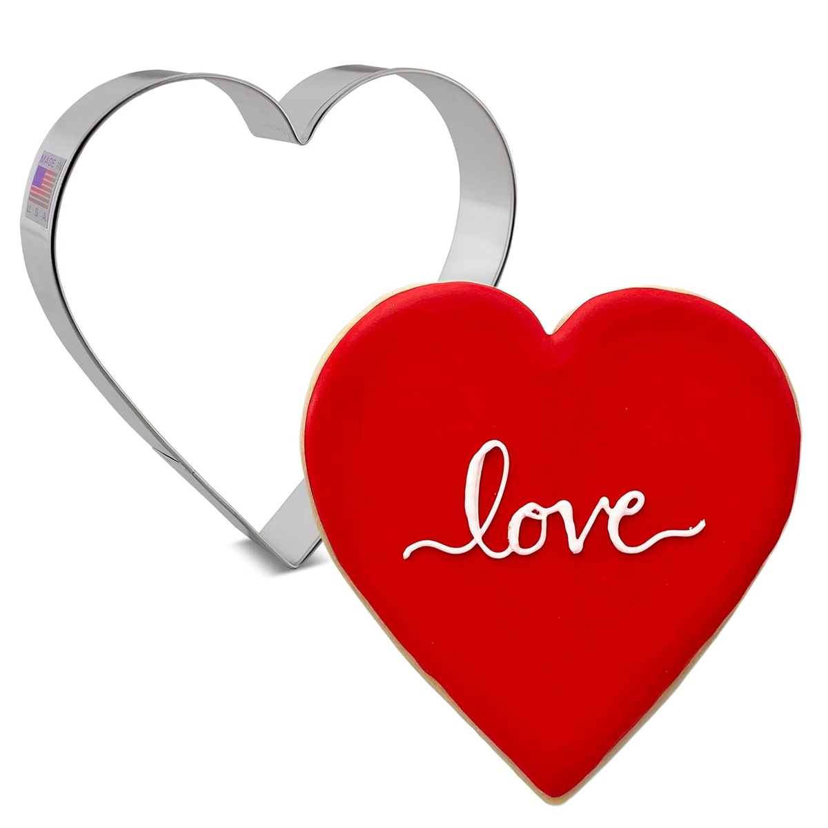 Extra large heart-shaped cookie cutter in polished silver steel next to a finished red heart-shaped cookie decorated with 'love' icing