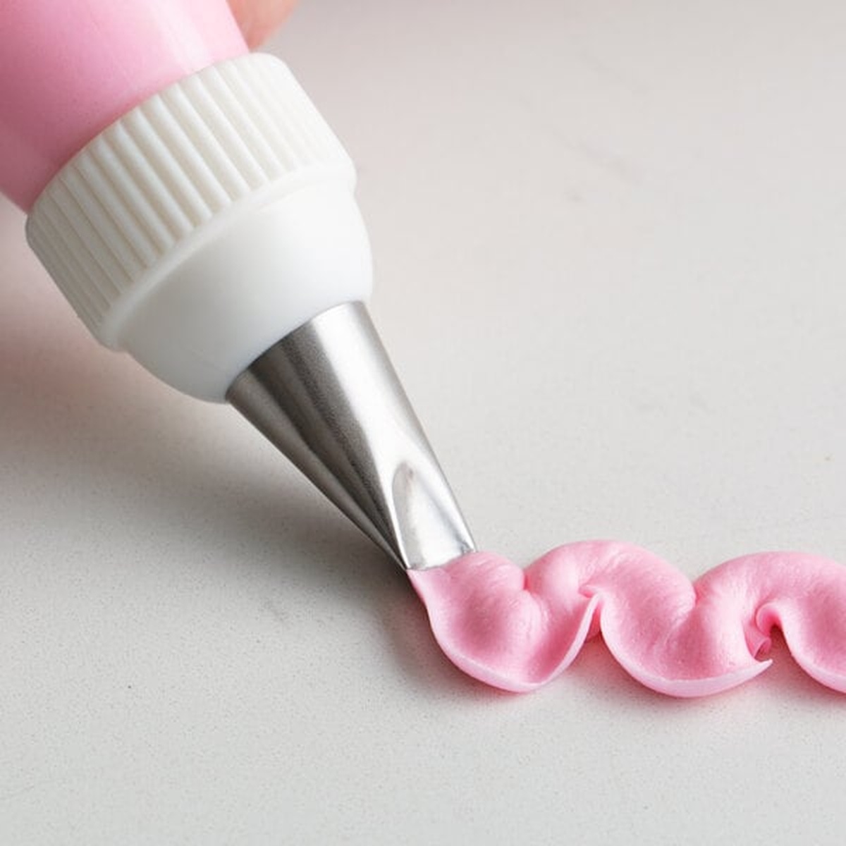 Ateco 120 piping tip attached to a pastry bag piping a curved petal border in pink frosting