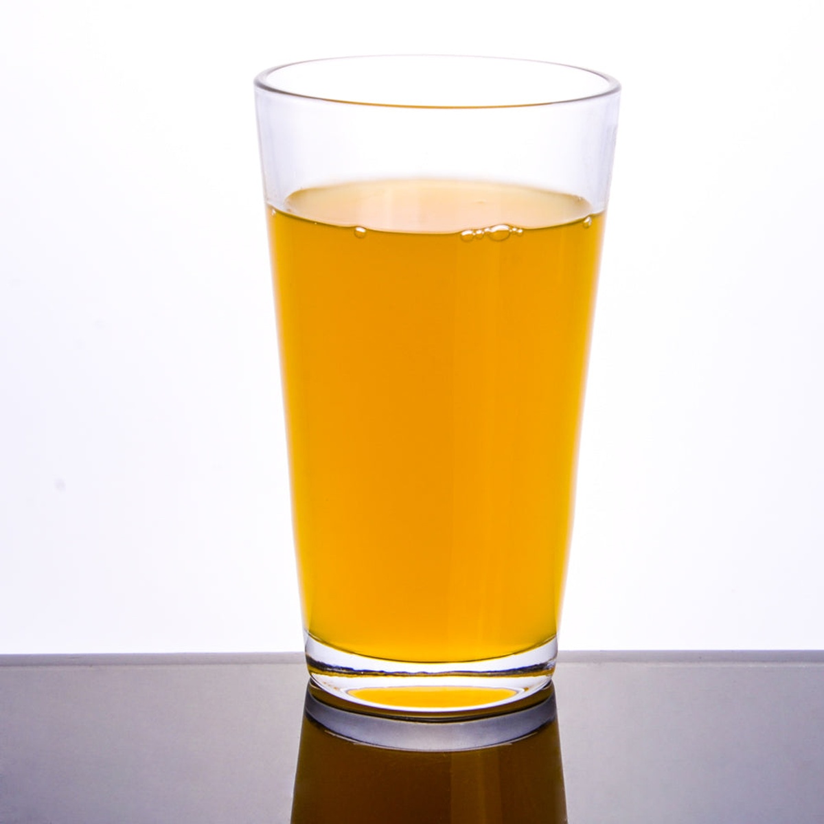 Enhanced Glassware 120 Enhanced 20 oz clear mixing glass filled with golden beverage on reflective surface