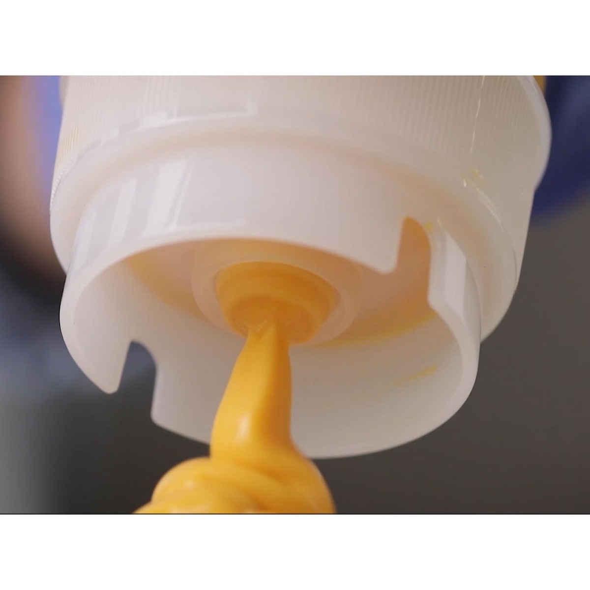Close-up of the InvertaTop ValveTop dispensing mechanism showing mustard flowing through the dual-opening valve