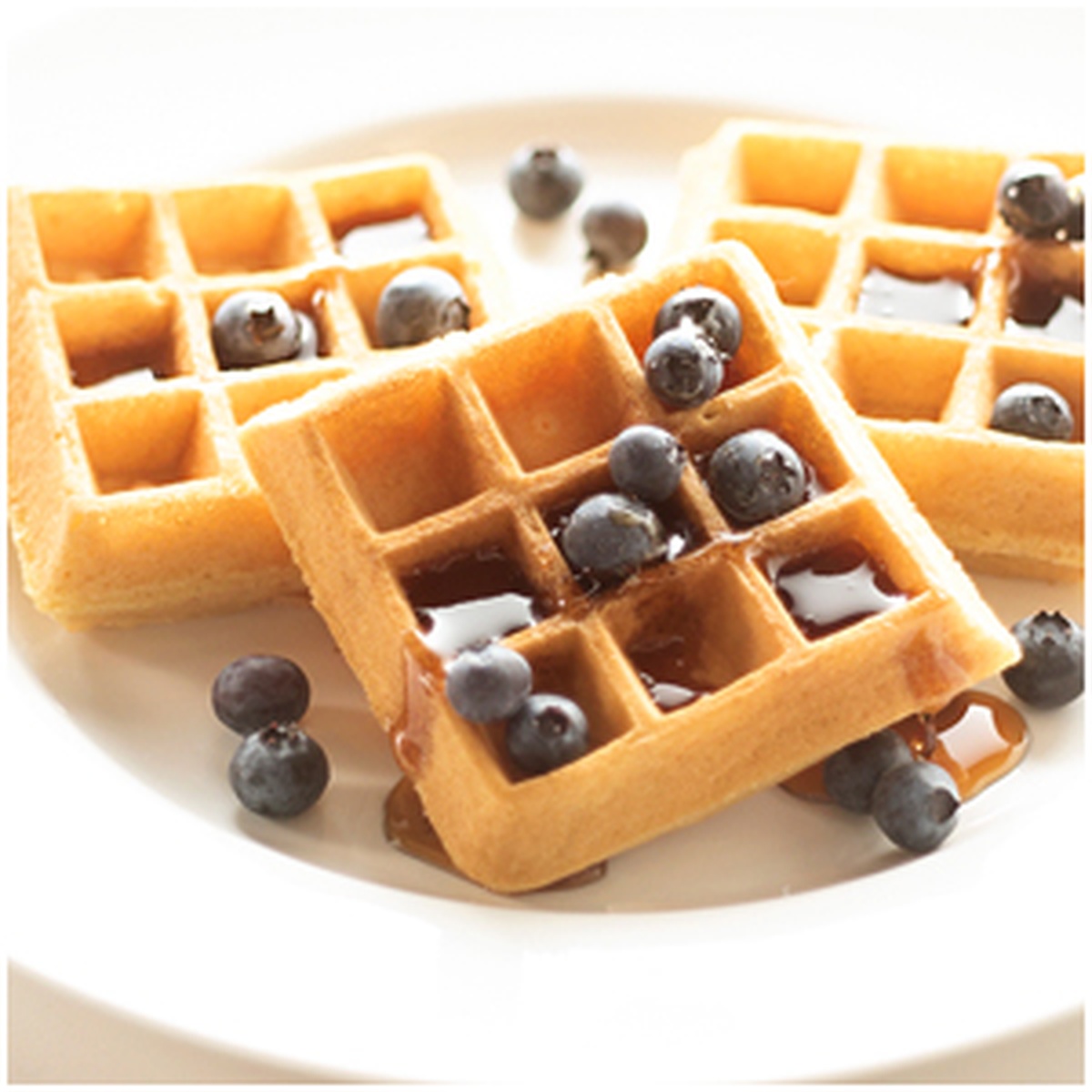 Golden Belgian waffles topped with blueberries and syrup on a white plate