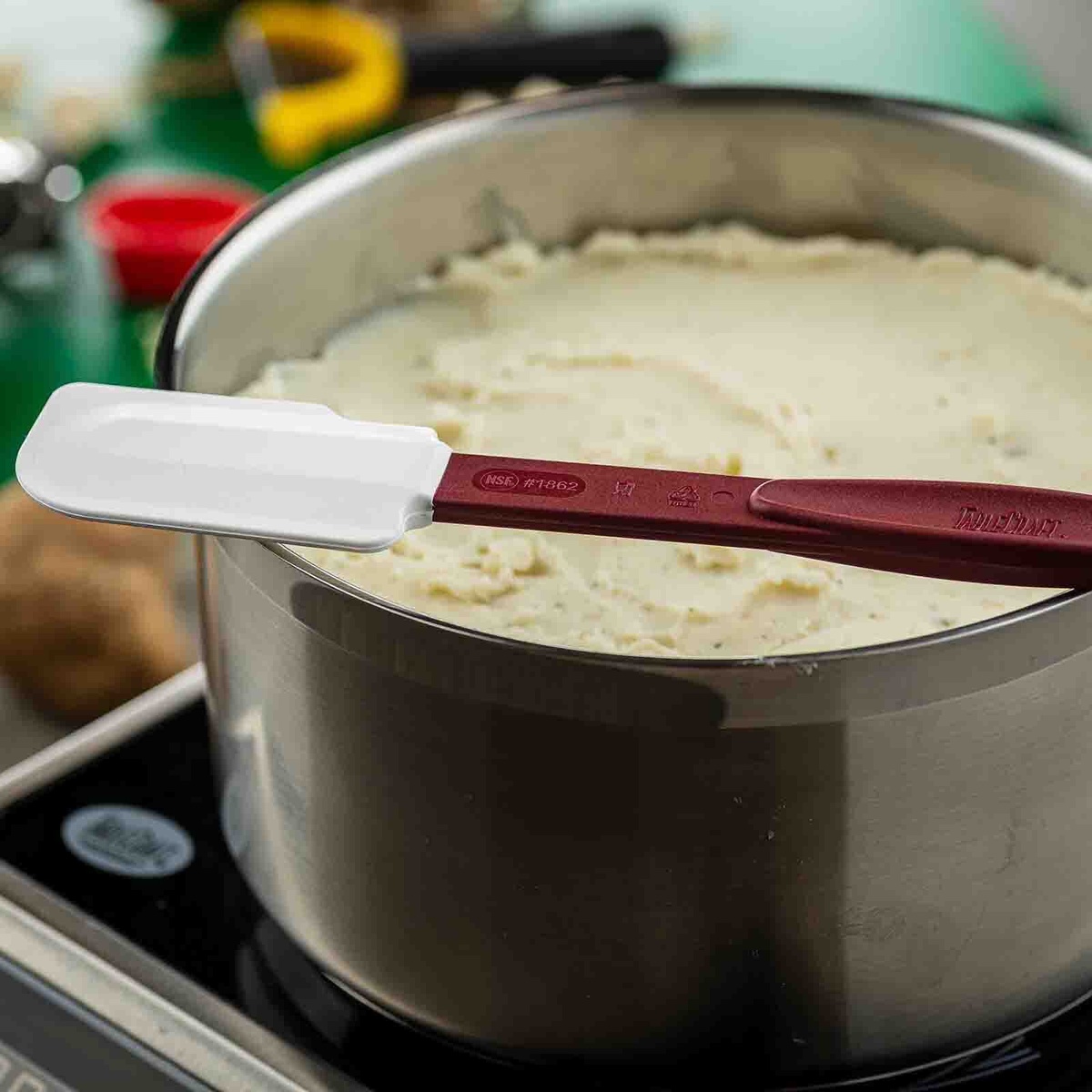 TableCraft 1862 high heat spatula balanced on rim of stainless steel pot on induction burner, showing silicone blade detail
