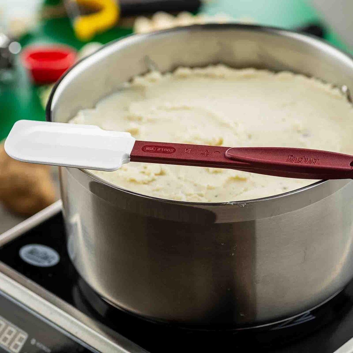 Close-up of TableCraft 1862 spatula with NSE marking resting on a pot of mashed potatoes on an induction cooktop