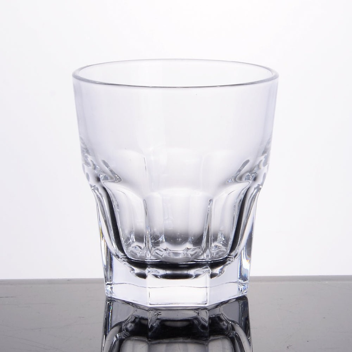 Enhanced 9 oz glass tumbler empty, showcasing its faceted base and tapered cylindrical form on a reflective surface