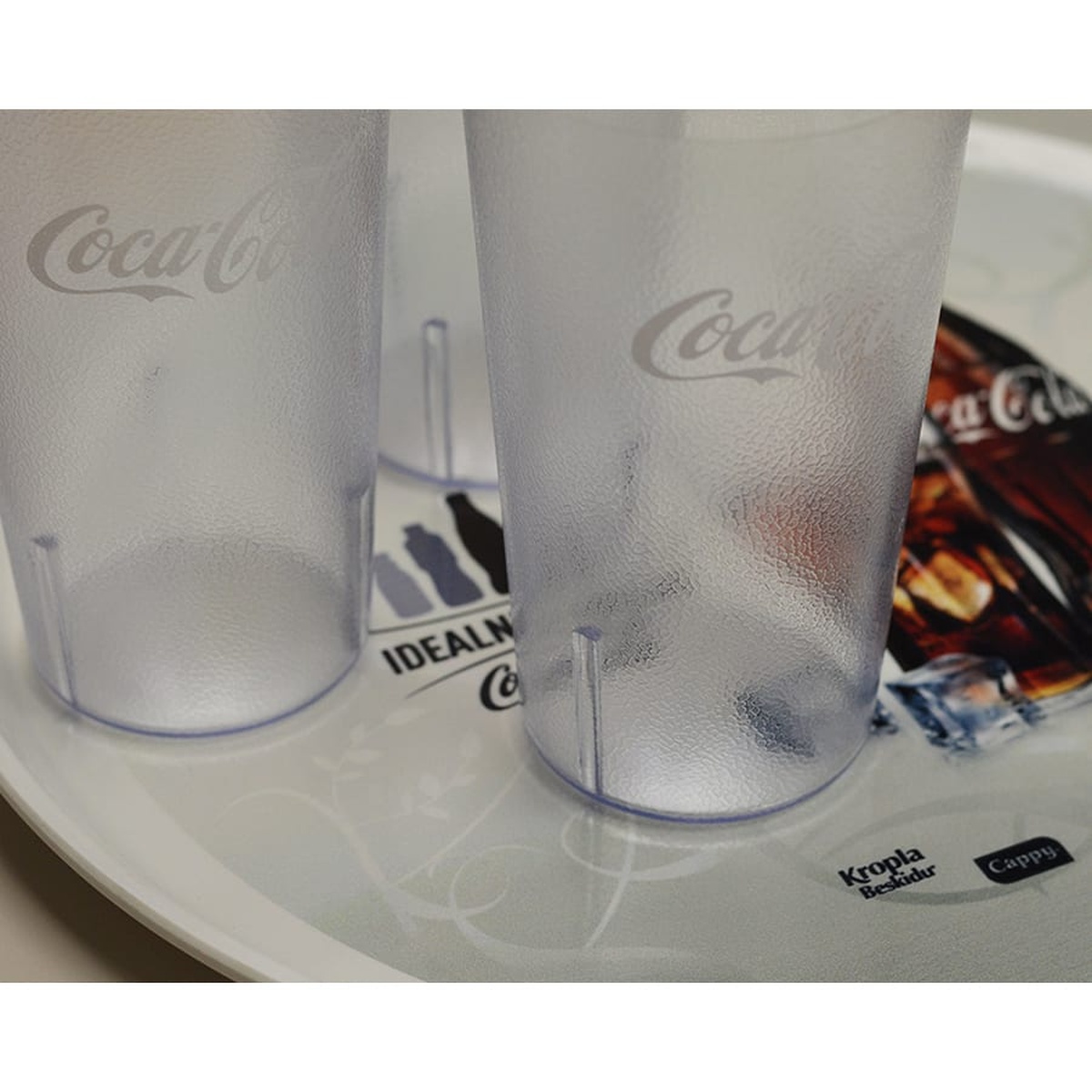 Bottom view of two Cambro clear SAN plastic Coca-Cola tumblers showing interior stacking lugs for space-saving storage
