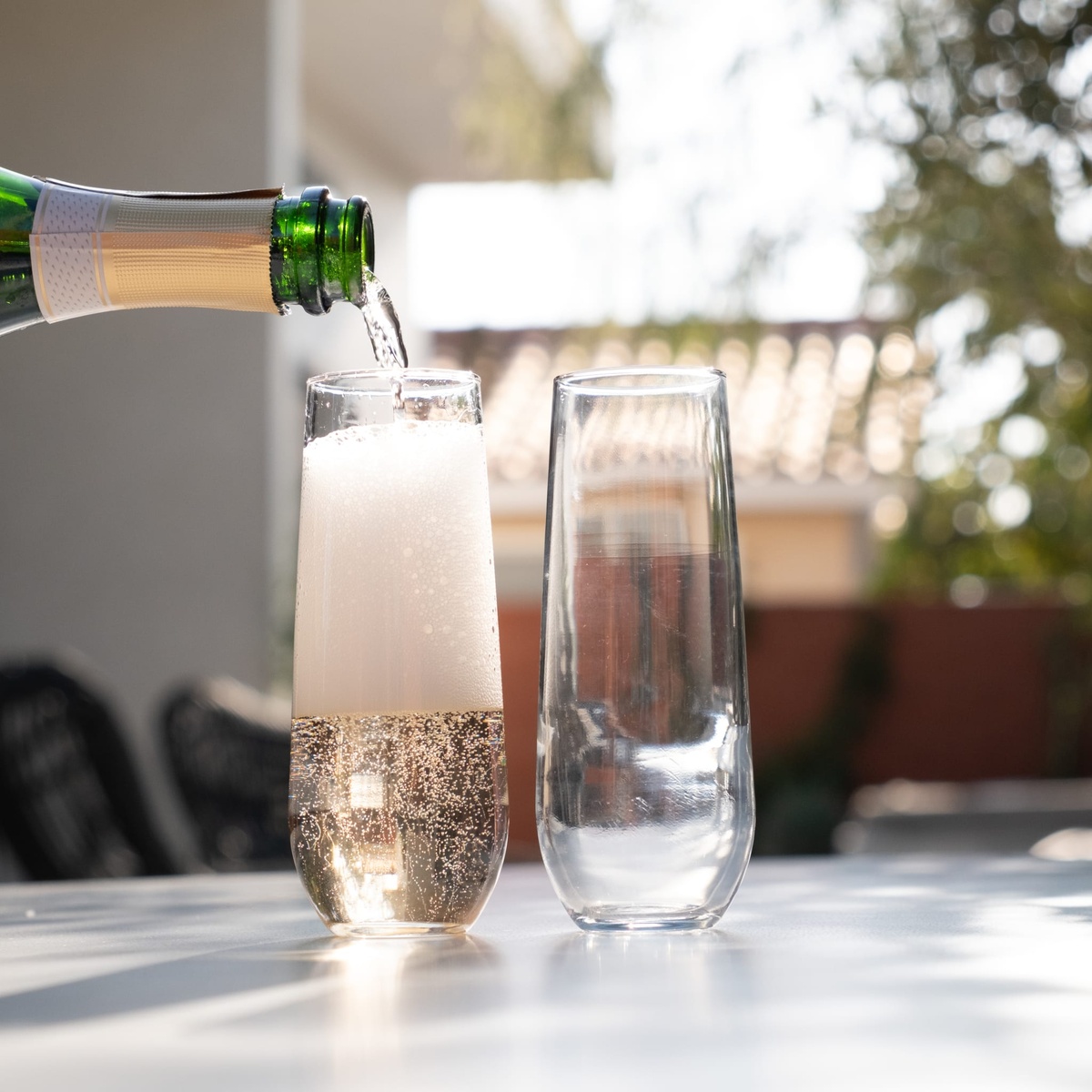 Champagne being poured from a bottle into a Libbey stemless flute glass on an outdoor table alongside an empty glass