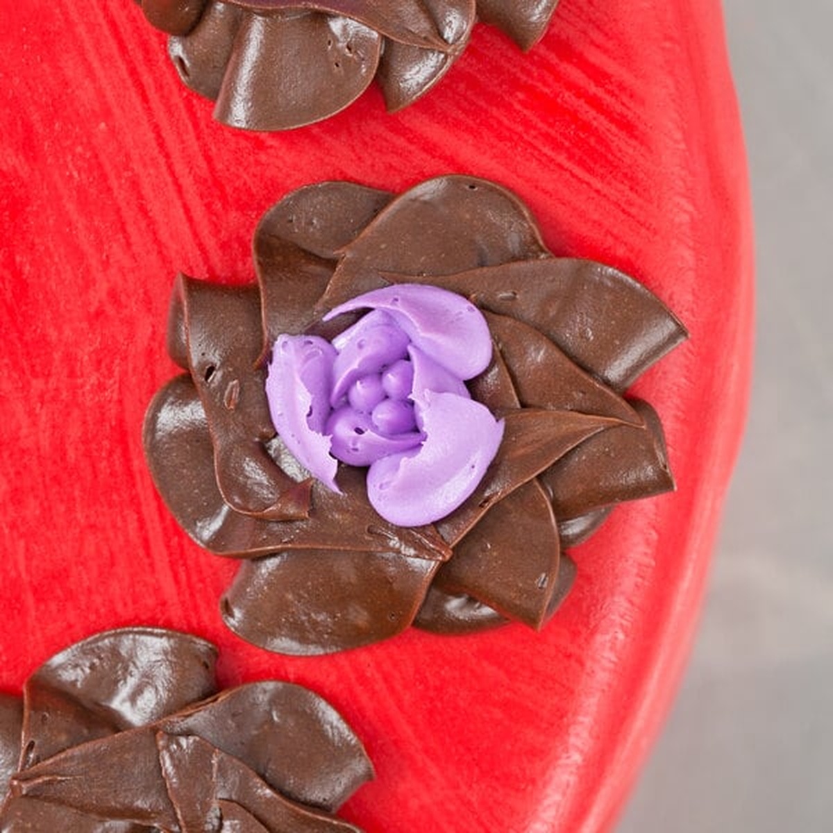 Chocolate and purple buttercream tulip flower decorations piped onto a red cake surface using the Ateco 242 tip