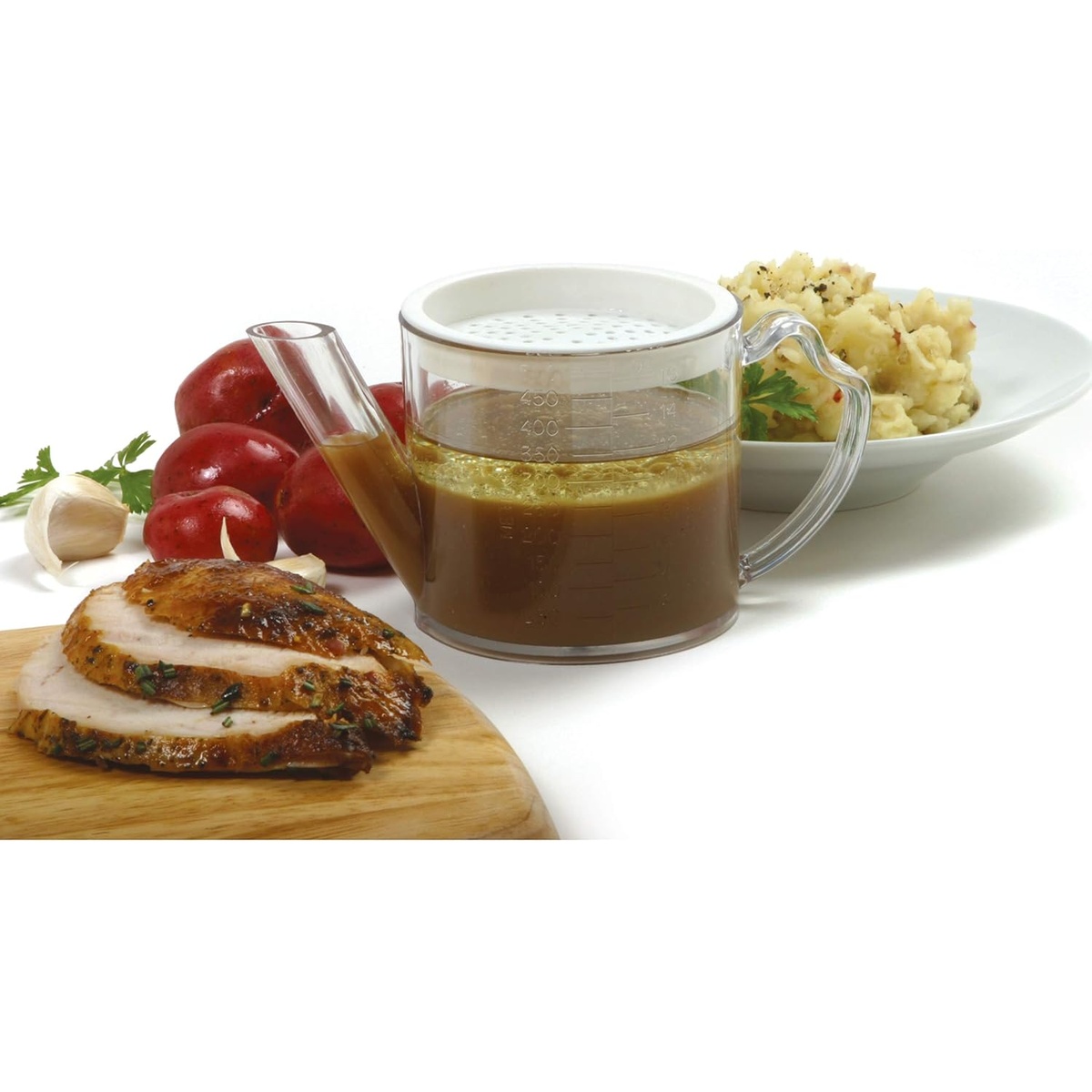 Norpro 3023 fat separator filled with separated gravy, displayed alongside sliced roast meat, red potatoes, and mashed potatoes