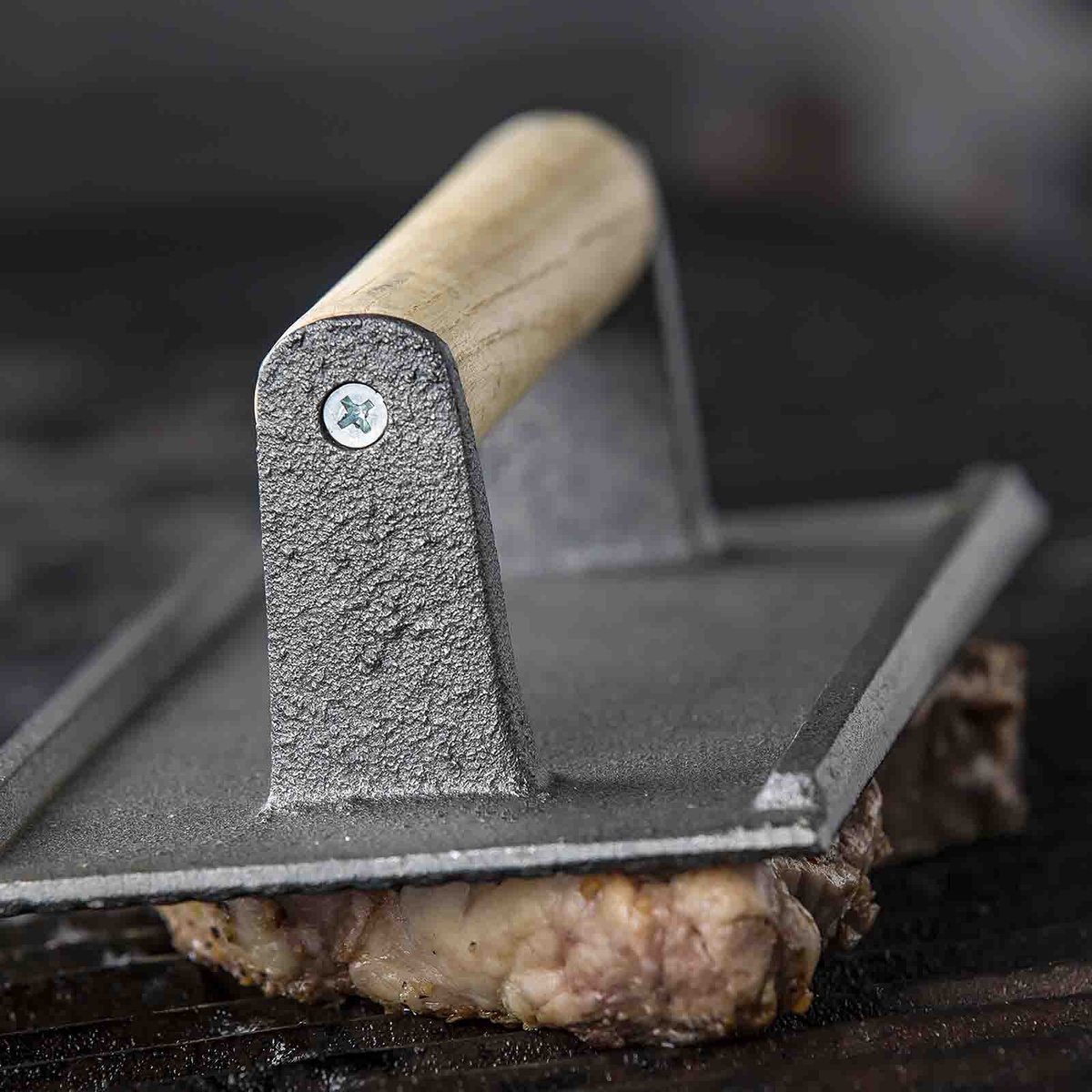TableCraft cast iron steak weight pressing meat on a commercial grill