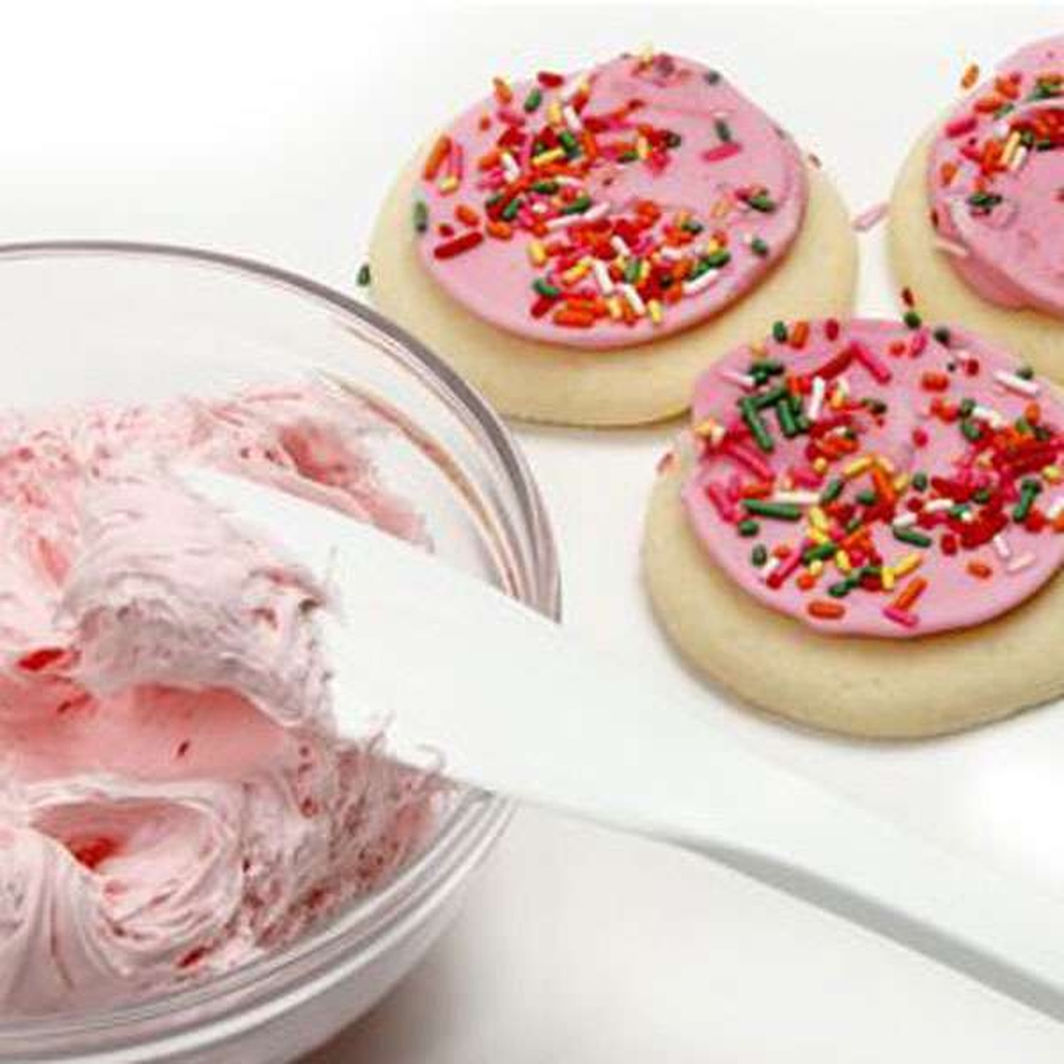 Norpro spatula scraper being used to frost decorated sugar cookies with pink frosting