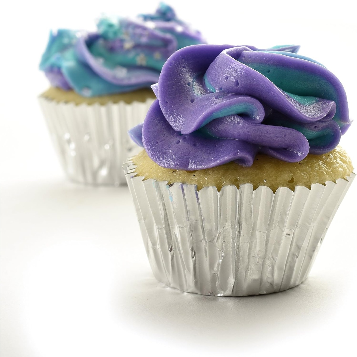 Two mini cupcakes with purple and teal frosting displayed in Norpro silver foil baking cups