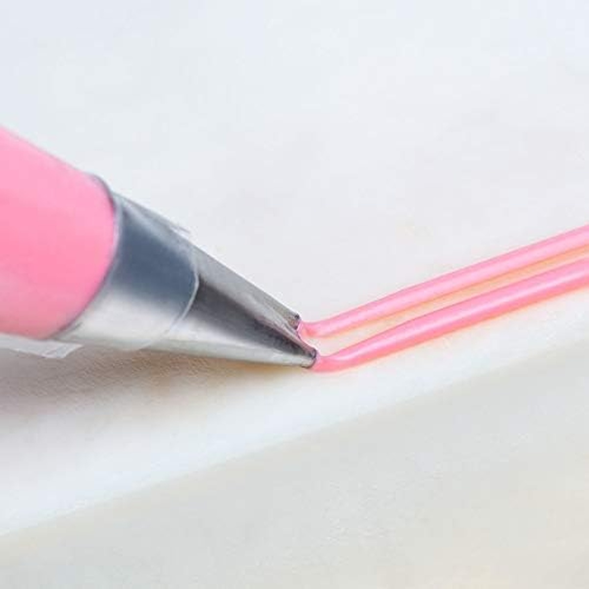 Ateco 42 piping tip in use piping two parallel lines of pink frosting on a white surface