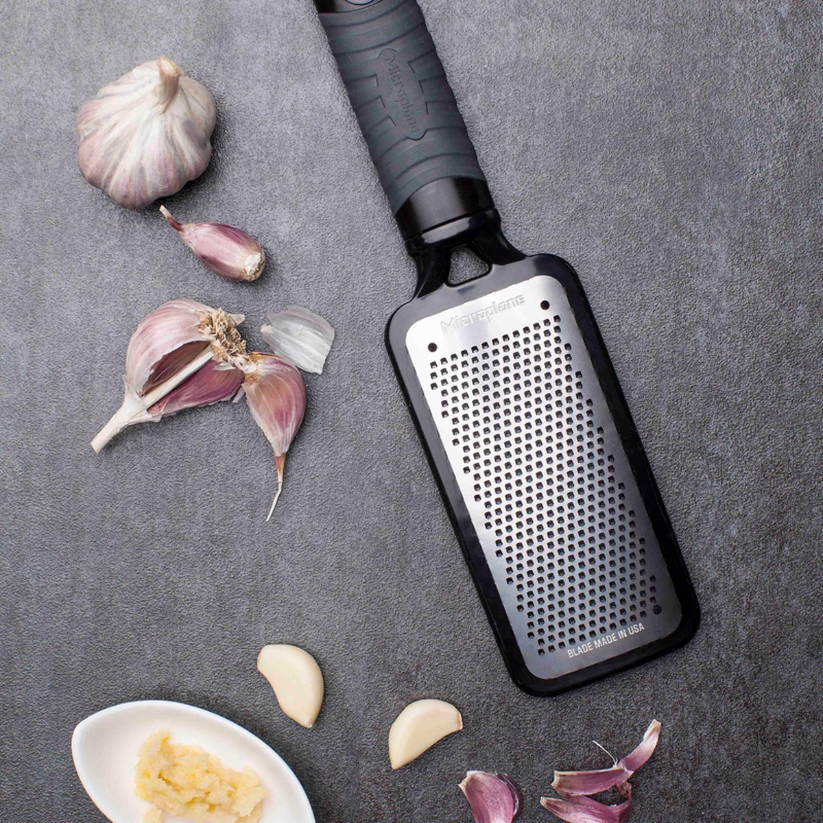 Microplane 44002 Fine Grater shown alongside fresh garlic cloves and minced garlic, blade detail visible