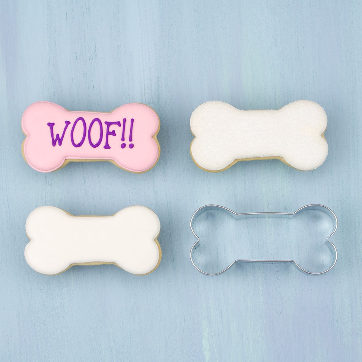 Decorated dog bone shaped cookies alongside a dog bone cookie cutter on a blue surface