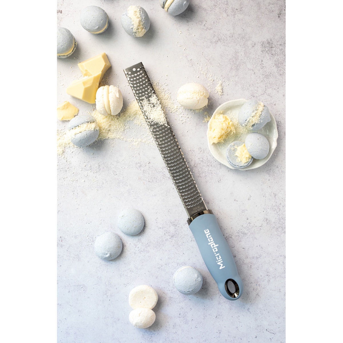 Microplane Sky Blue Zester Grater on a light surface with macarons and white chocolate
