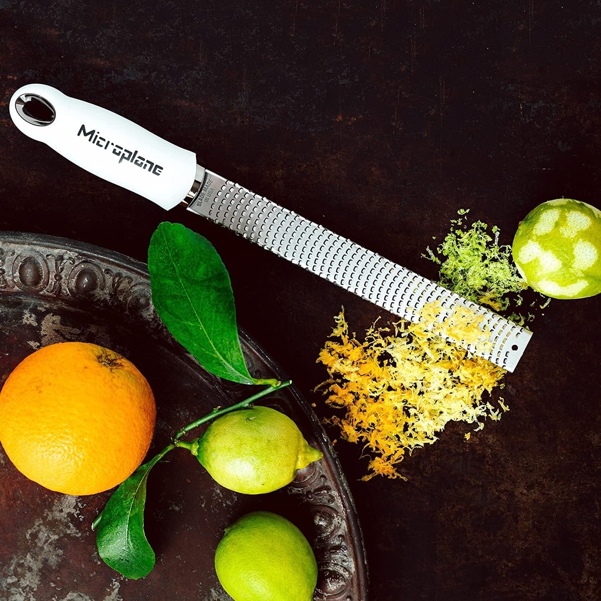 Microplane zester being used to zest a fresh lemon over a dark surface