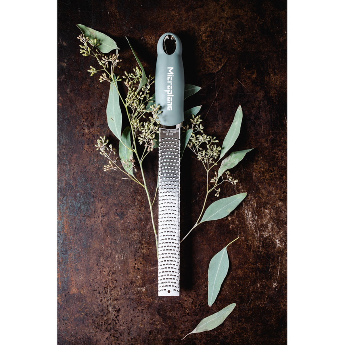 Microplane 46727 Zester Grater in Eucalyptus Green with stainless steel blade on a rustic dark surface with eucalyptus leaves