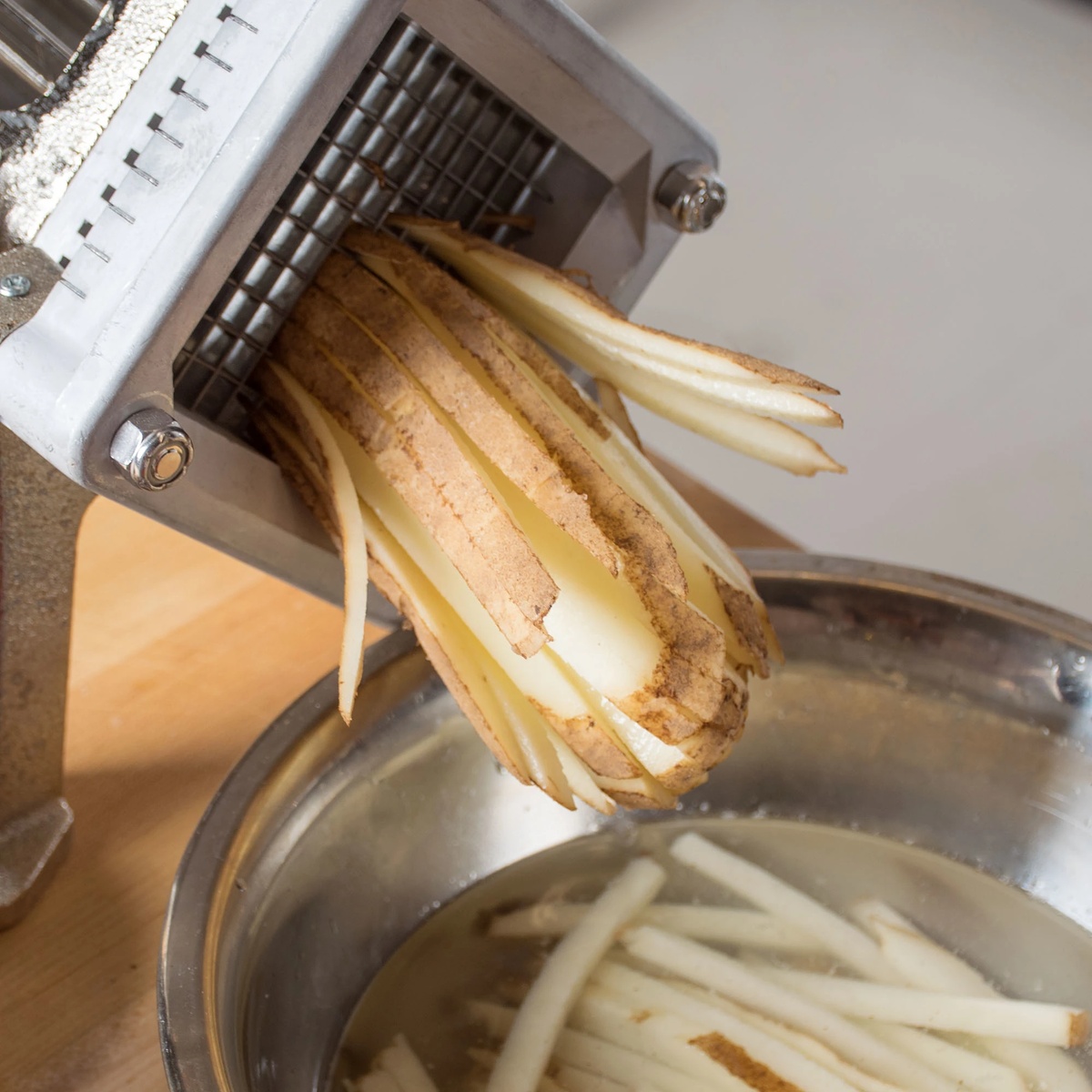 Close-up view of potato being cut into uniform french fries through the stainless steel V trough blade assembly