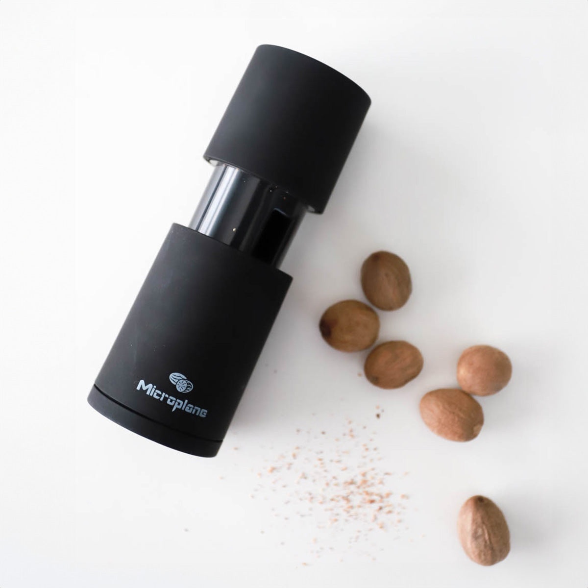 Black manual spice mill standing next to whole nutmeg seeds and freshly ground spice particles