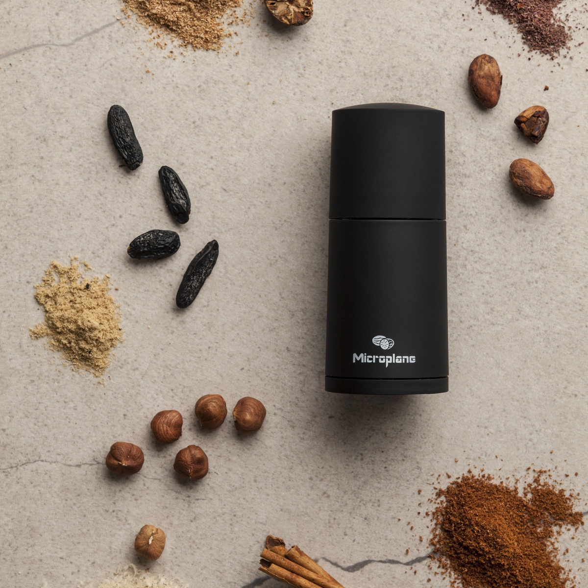 Overhead view of the Microplane spice mill surrounded by various whole and ground spices