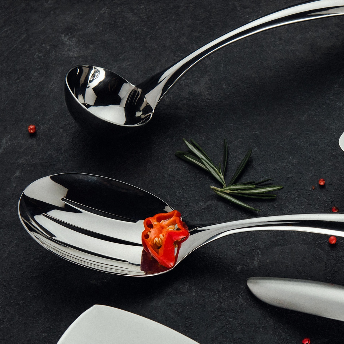 Browne Eclipse stainless steel serving ladles and spoons arranged on a dark stone surface