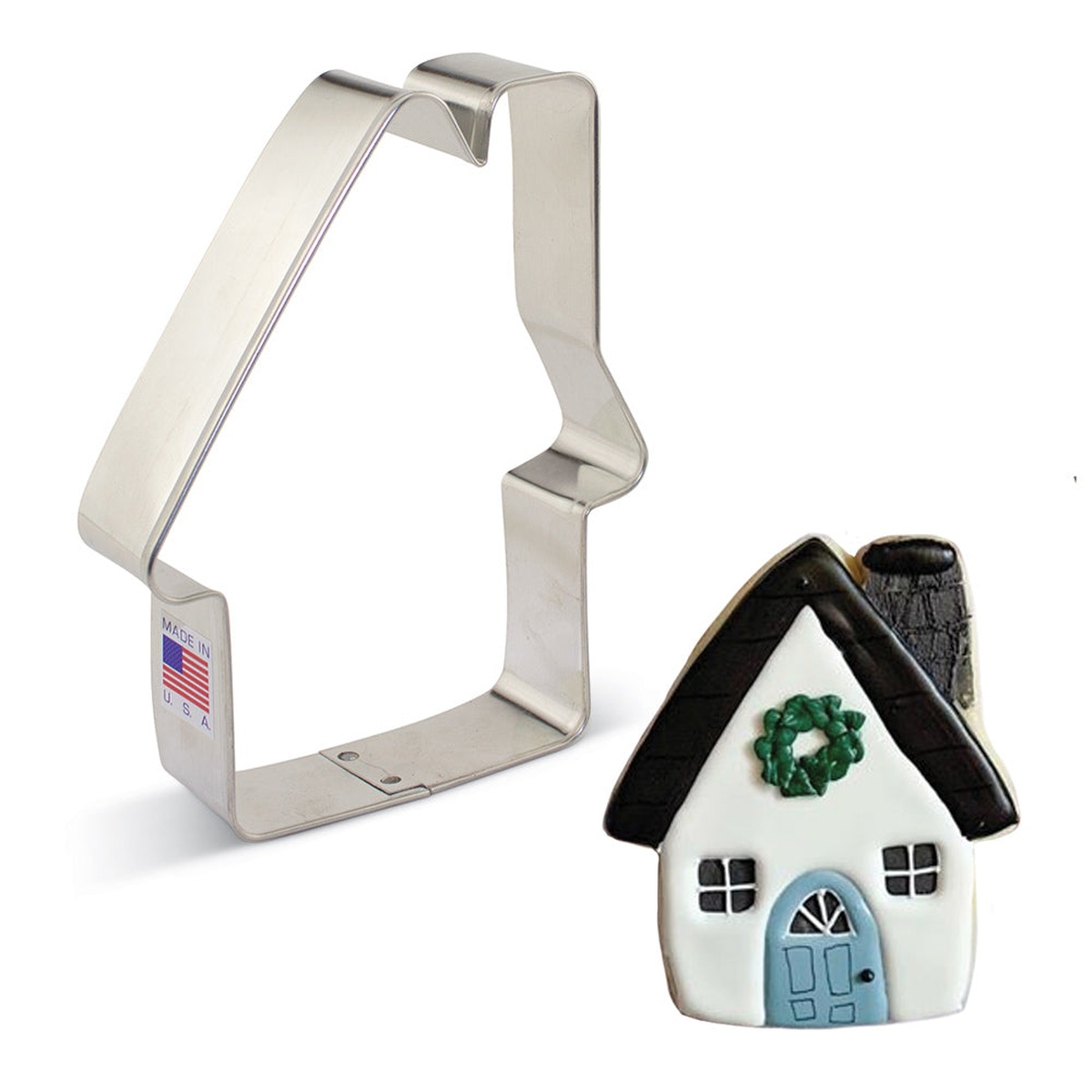 Gingerbread house cookie cutter shown alongside a decorated house-shaped cookie with white icing, black roof, and a green wreath