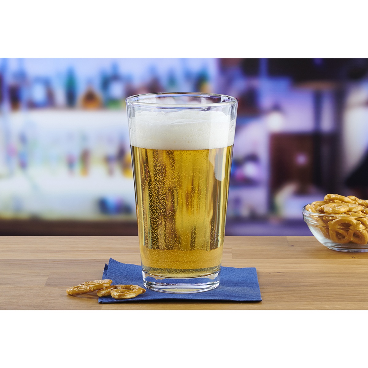 Anchor Hocking 16 oz. Mixing Glass filled with lager beer, placed on a blue napkin beside pretzels