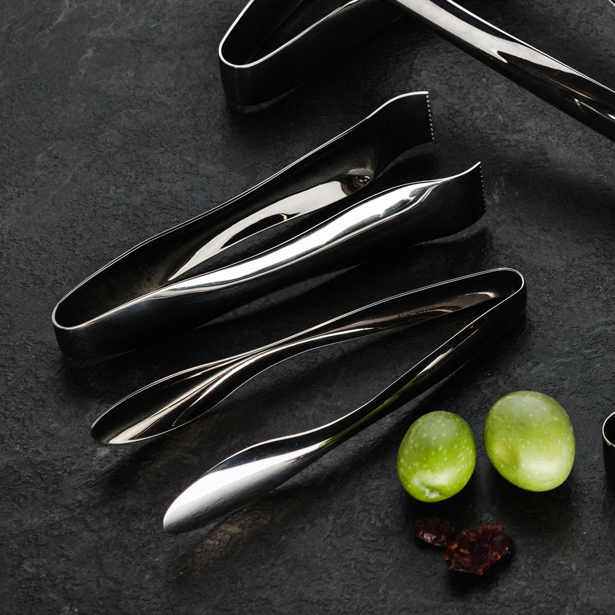 Multiple Browne Eclipse Serving Tongs in mirror and satin polished stainless steel displayed on dark slate surface