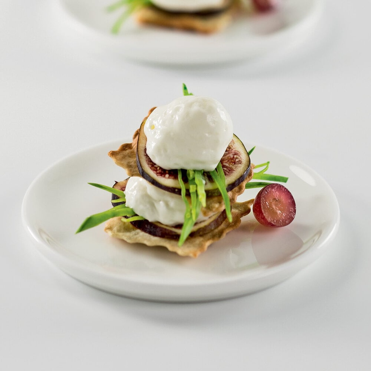 Gourmet appetizer plated with whipped cream topping, figs, greens, and a grape, demonstrating savory use of the whipped cream dispenser