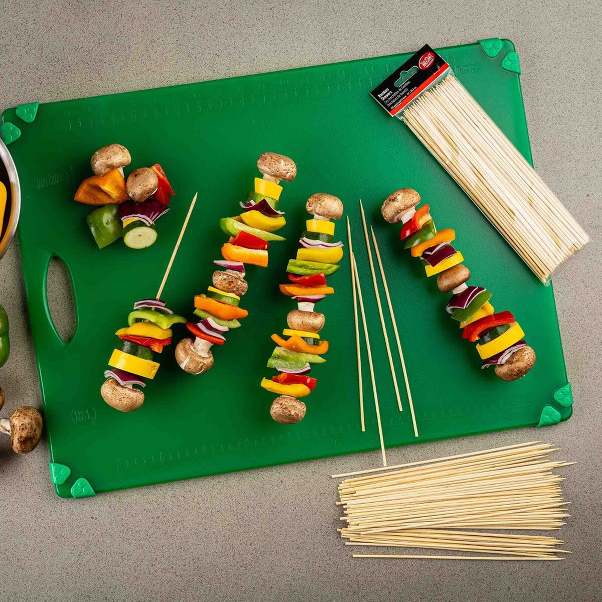 Bamboo skewers arranged with fresh vegetables on a green cutting board