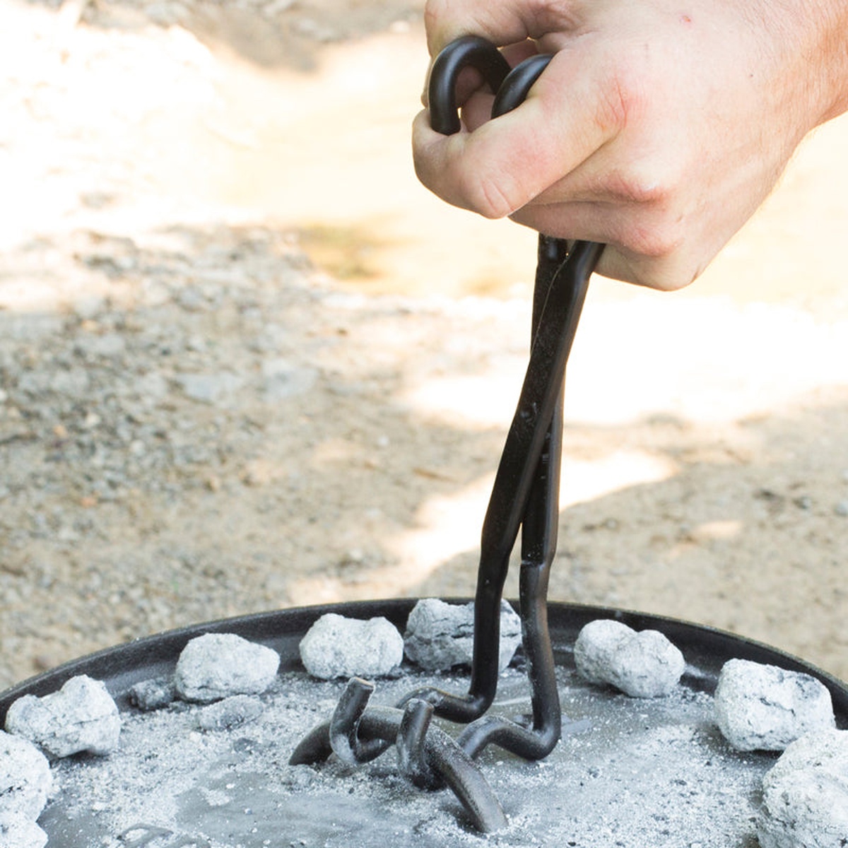 Lodge 4-in-1 tool being used to lift a hot Dutch oven lid covered in charcoal