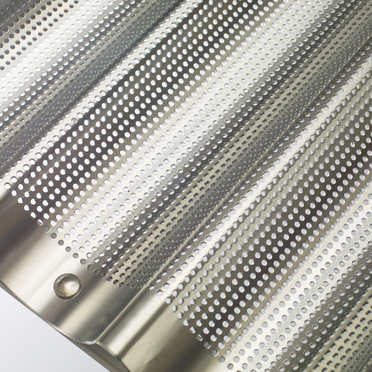 Close-up detail of the perforated aluminum surface and riveted corner of the Winco baguette pan