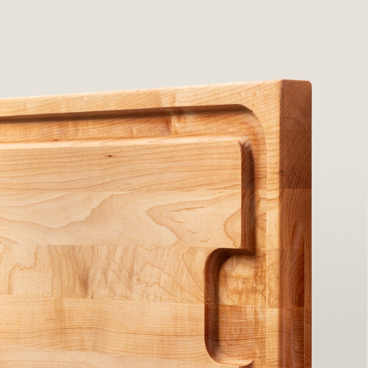 Close-up detail of John Boos AuJus maple cutting board showing precision-carved juice groove and recessed finger grip