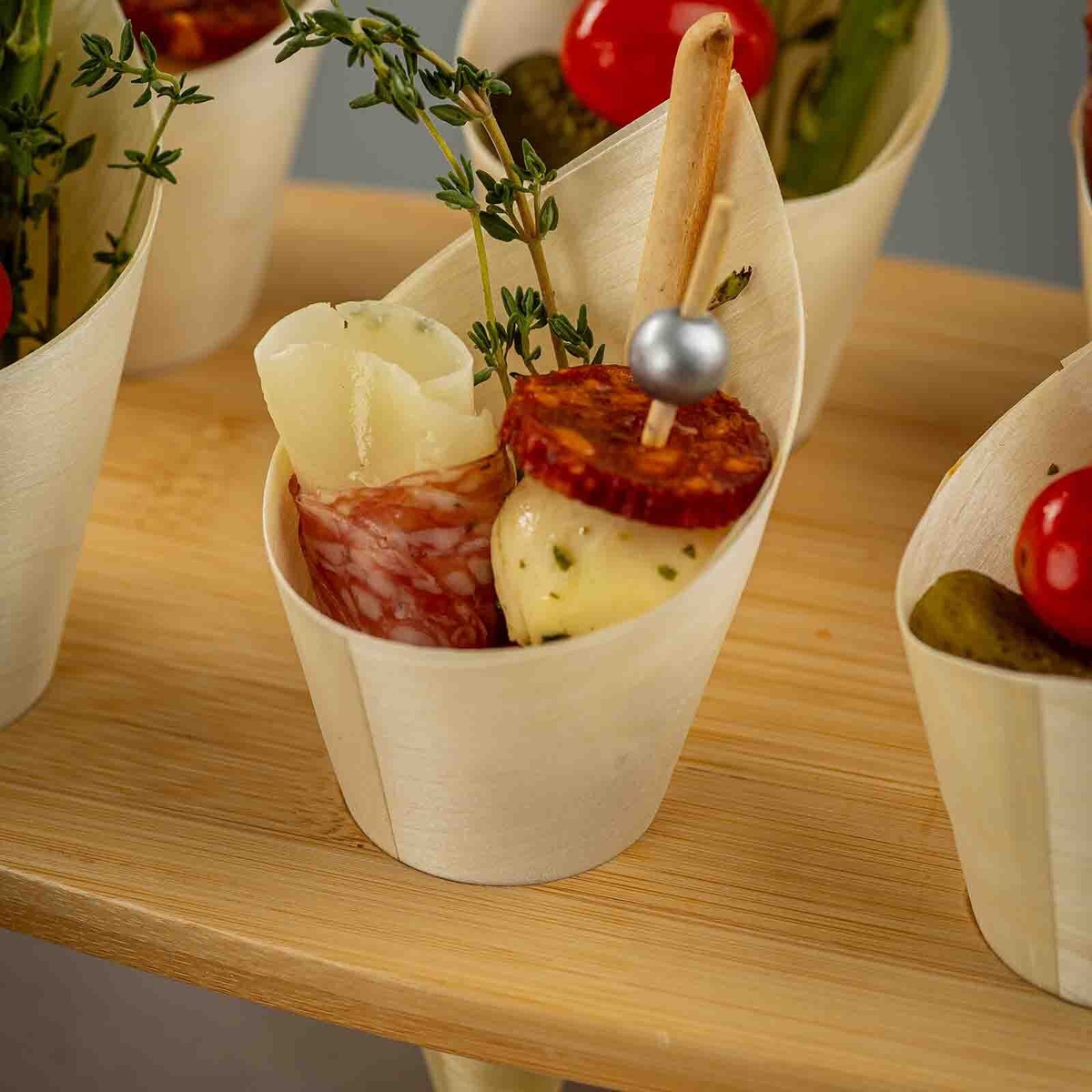 Close up of a wooden serving cone filled with charcuterie appetizers including cheese and meat