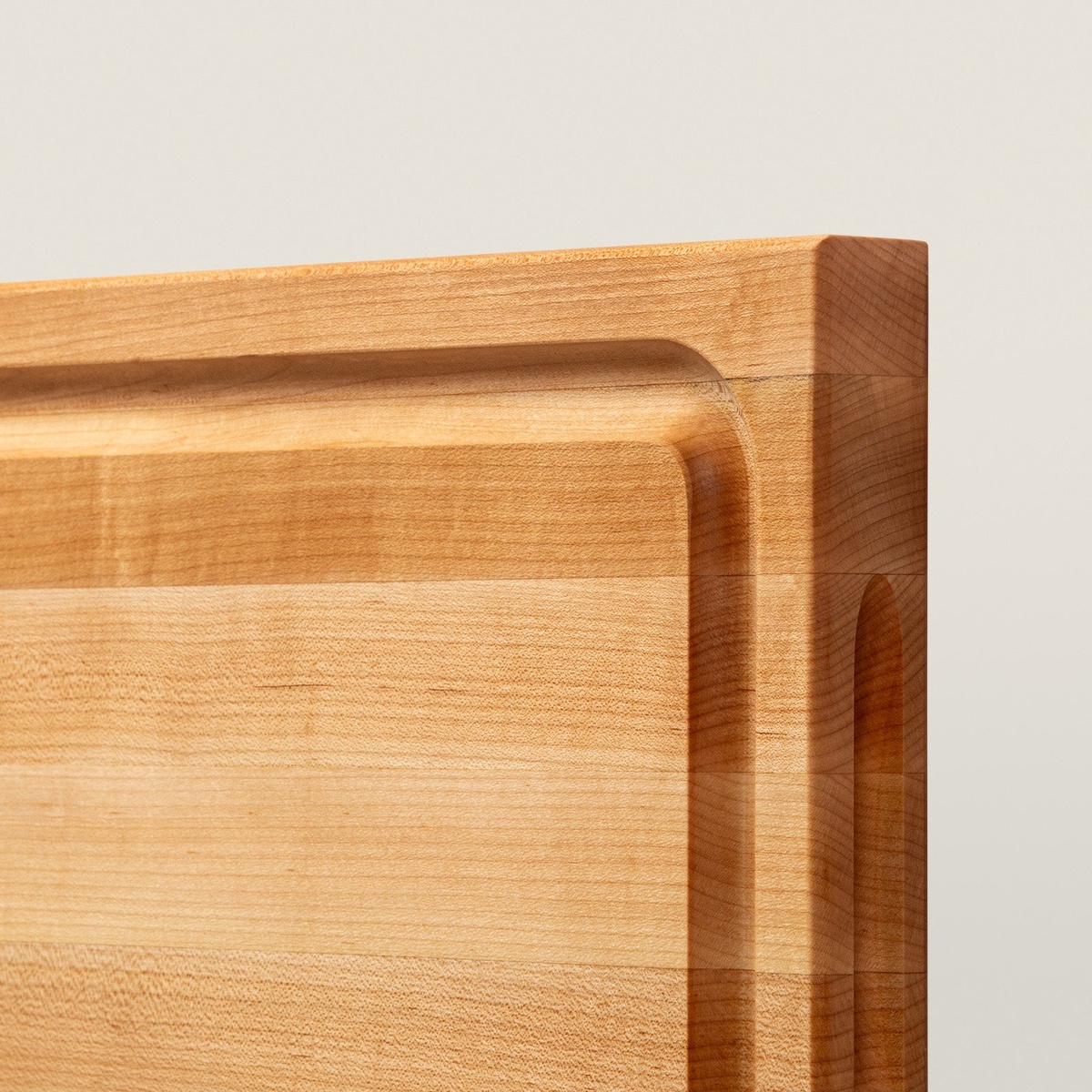 Close-up detail of the carved juice groove and finger grip cutout on the John Boos BBQBD maple cutting board corner